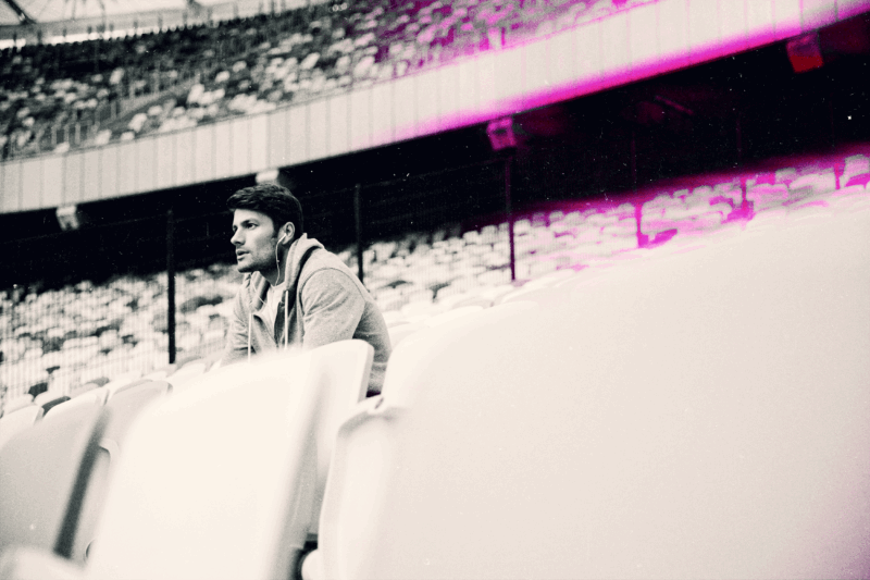 Serious young man sat at an empty sports stadium listening to headphones