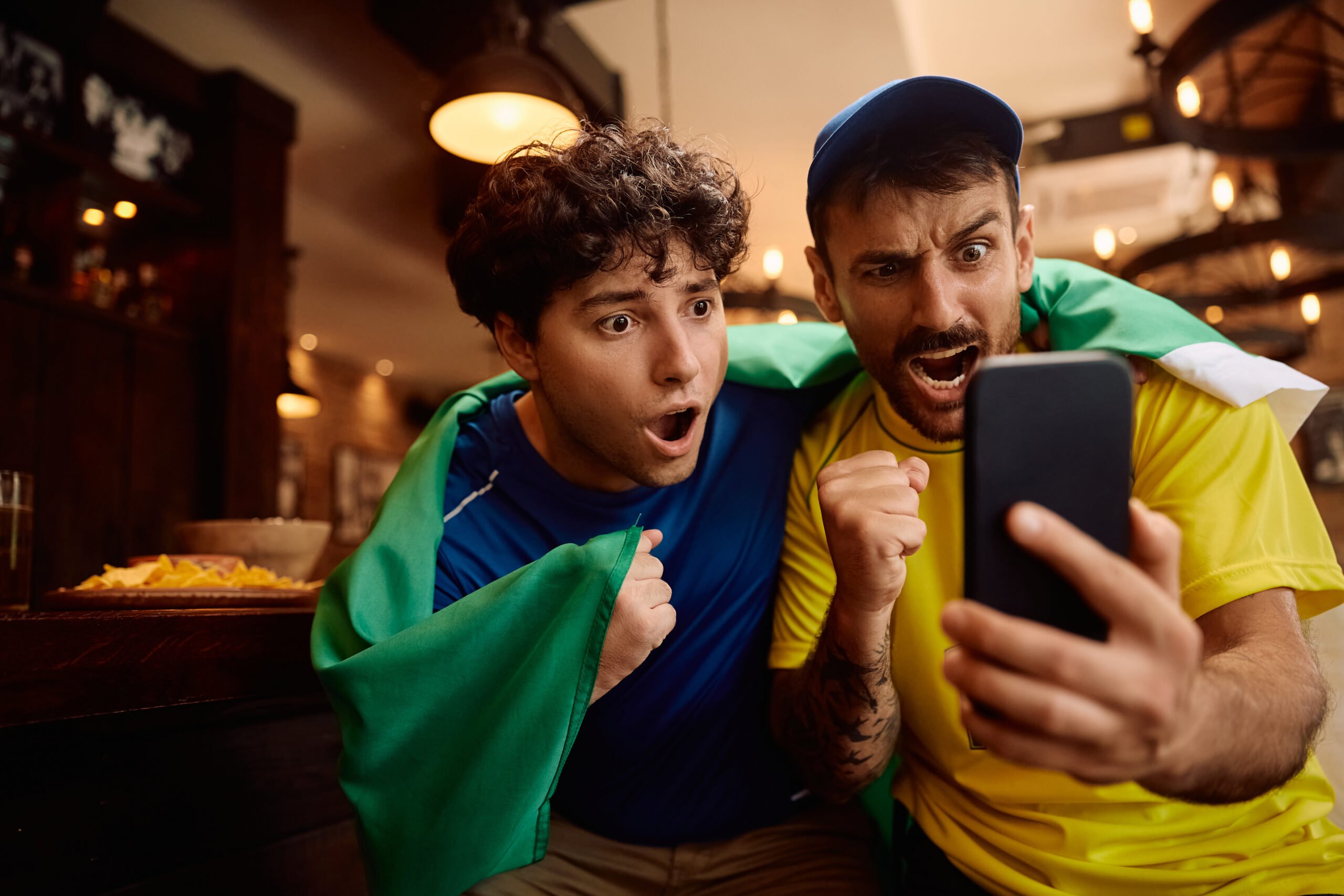 Two exited fans engaging with a sports game they're watching on their phones