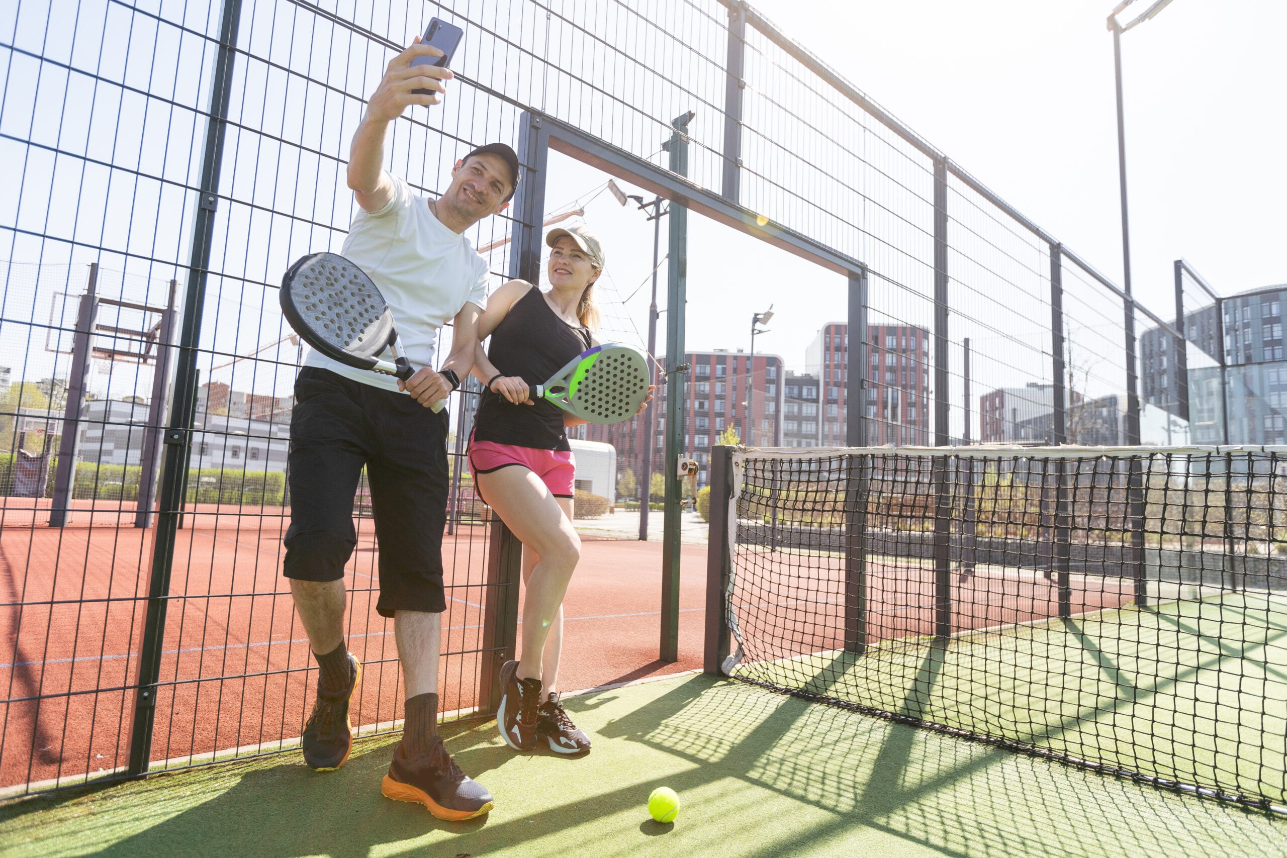 Portrait of positive young woman and adult man standing on padel tennis court, holding racket and ball, smiling. 