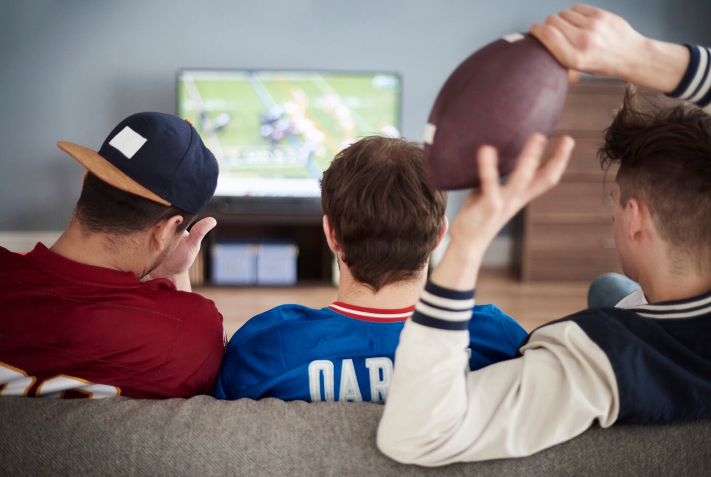 Rear view of male friends watching sports on tv on the background