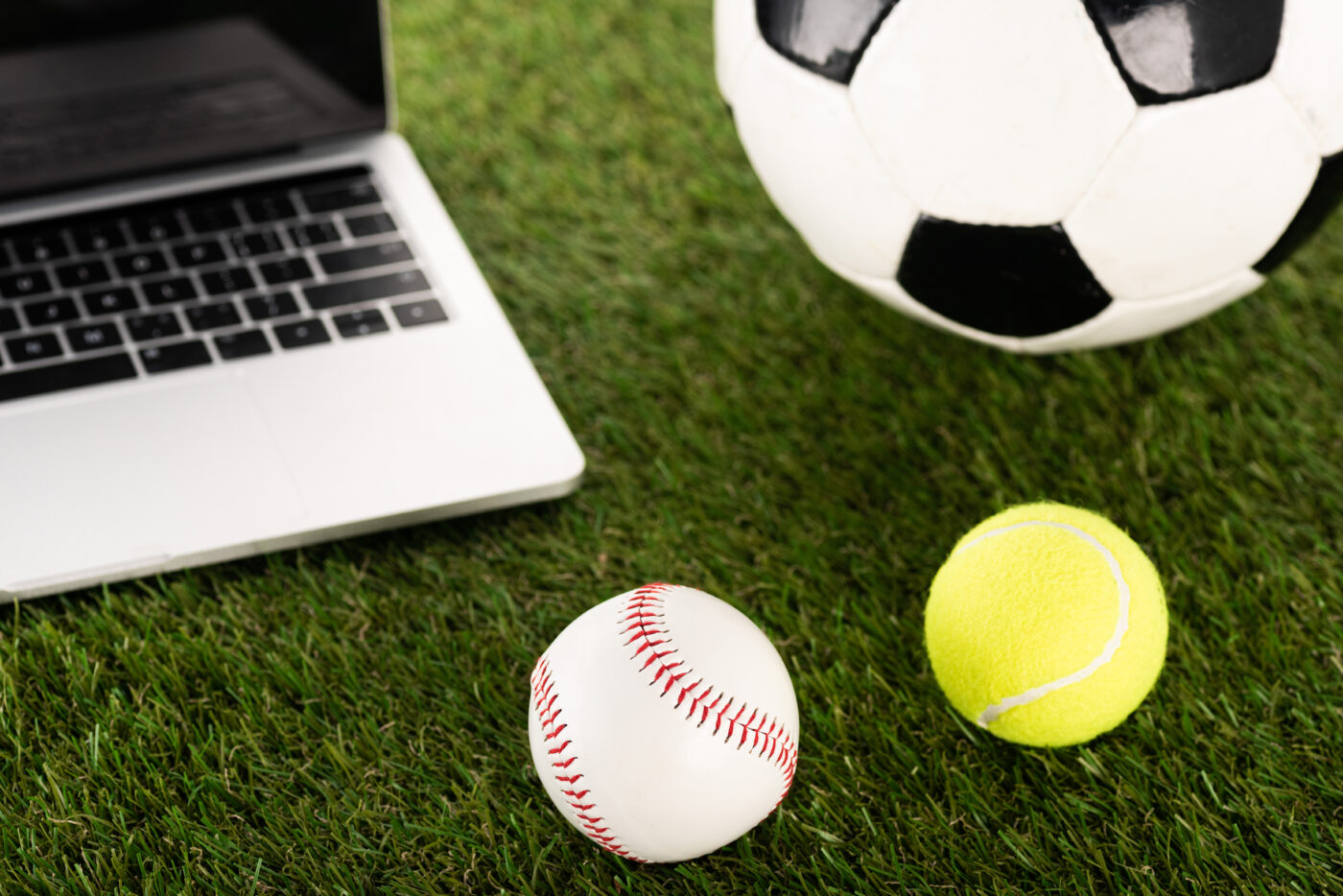 soccer baseball and tennis balls near laptop on grass