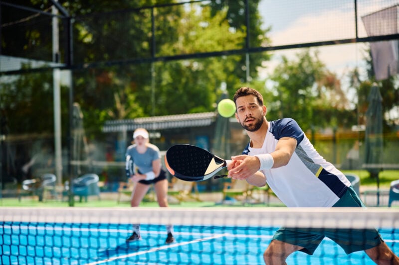 Paddle tennis player hitting the ball during mixed doubles match on outdoor court.