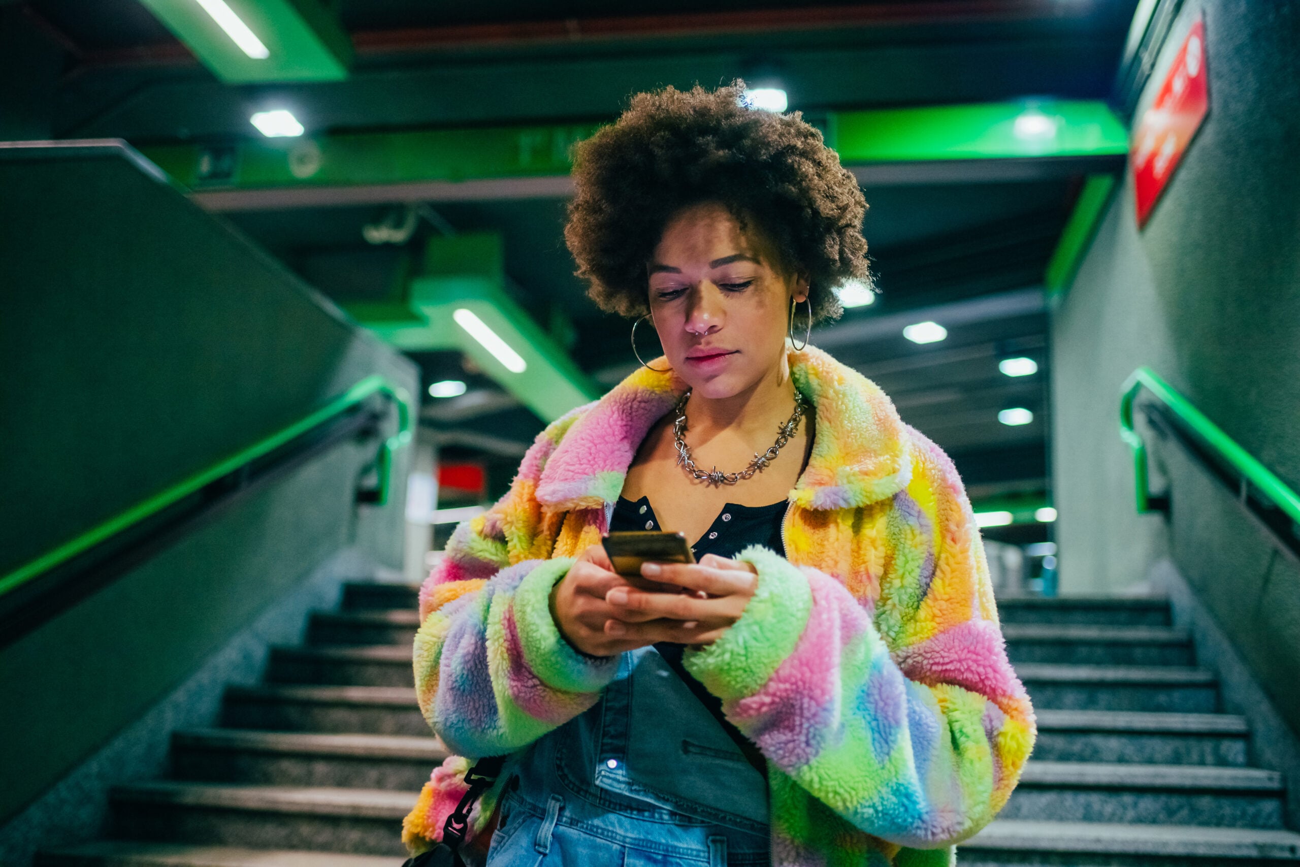 Young mixed race woman indoor metro station using smartphone surfing web shopping online