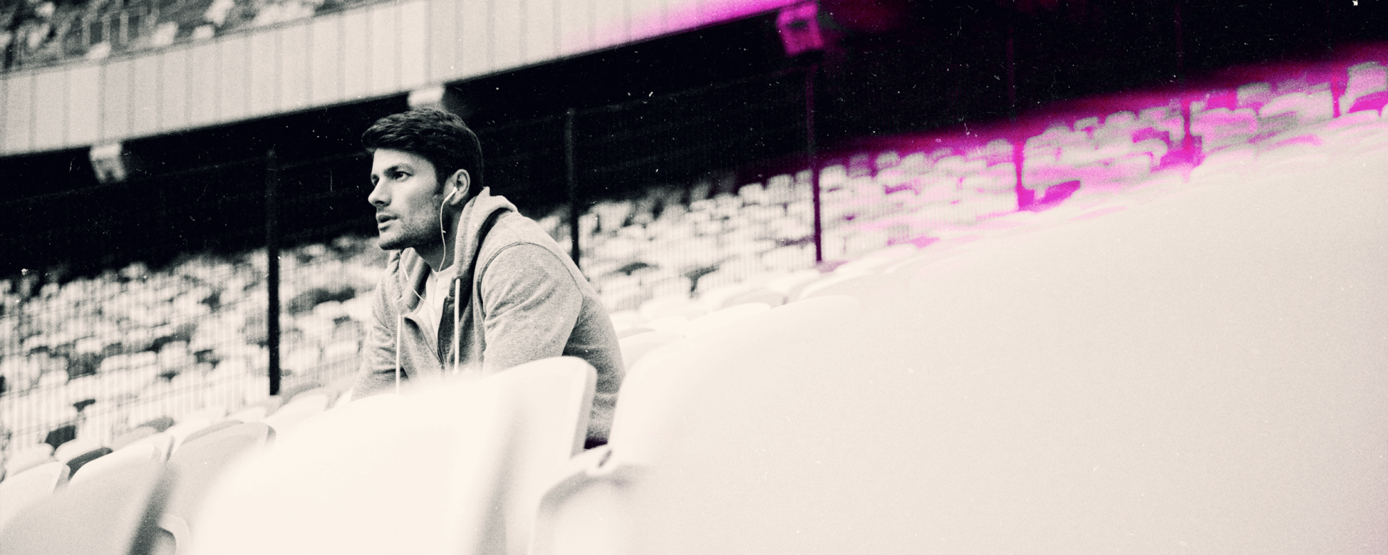 Serious young man sat at an empty sports stadium listening to headphones