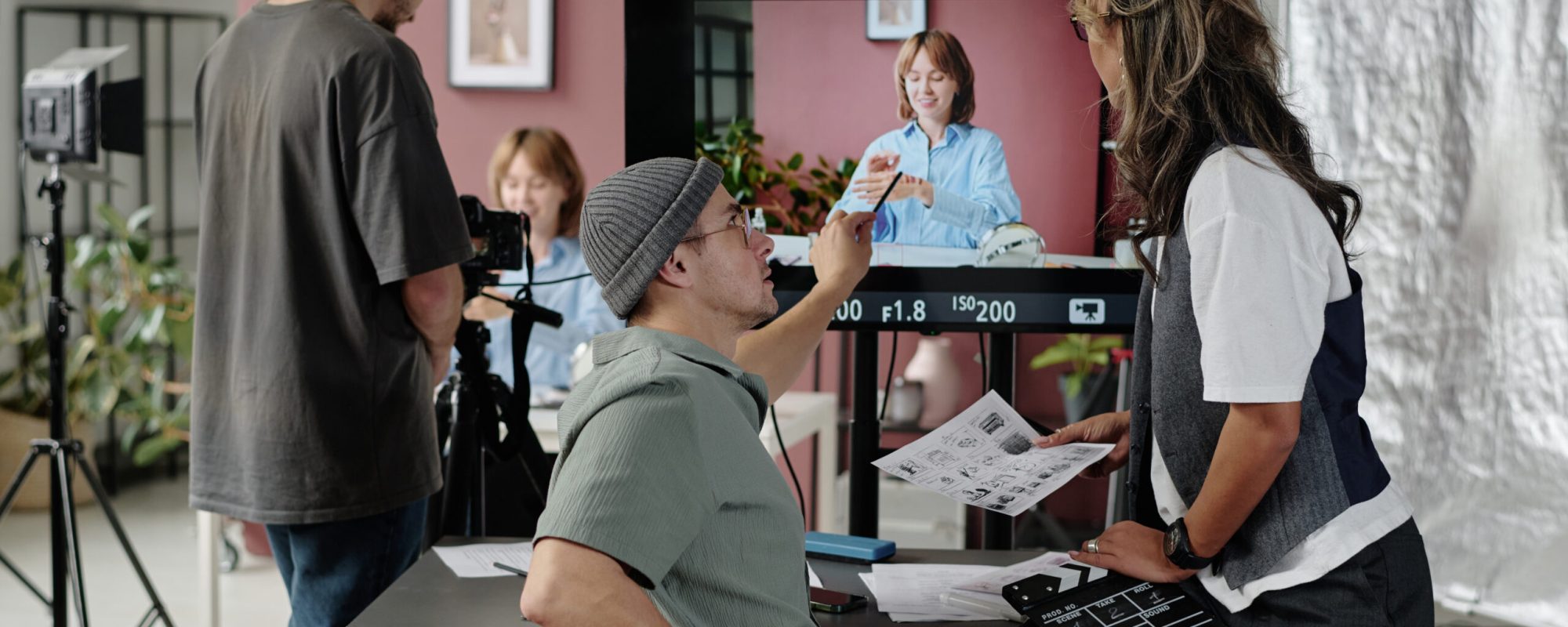 Male professional director discussing essential props with assistant director who looking at big screen while operator setting camera