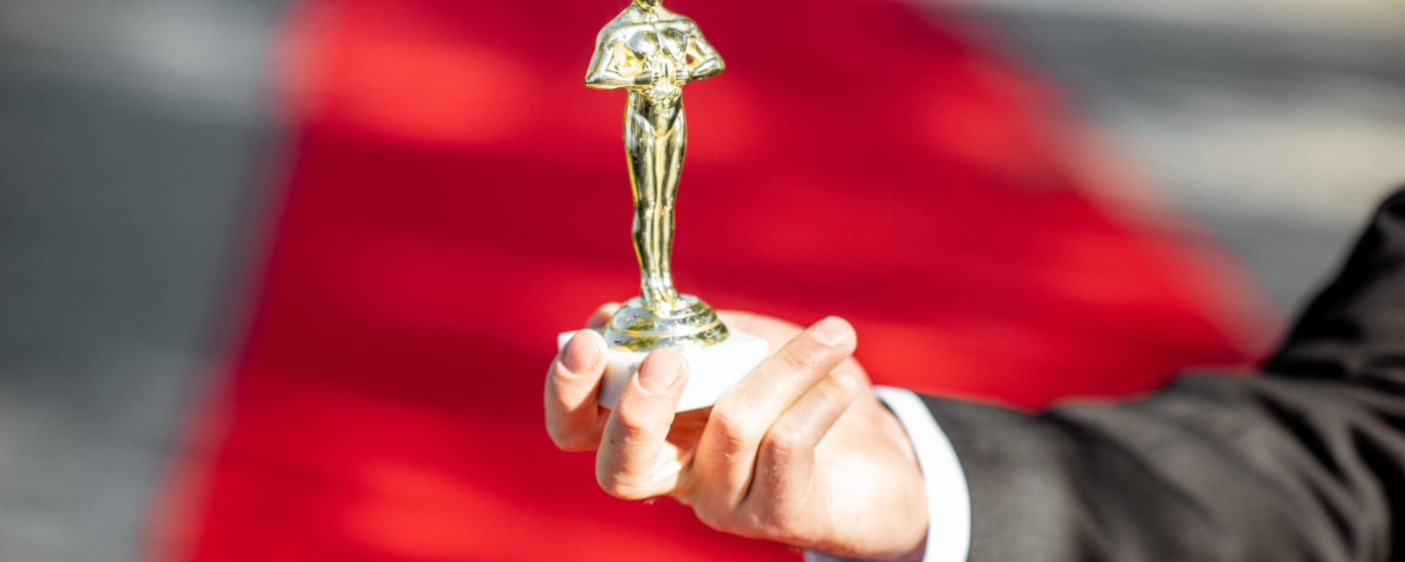 Man holding famous film award statue on the red carpet background, close-up view