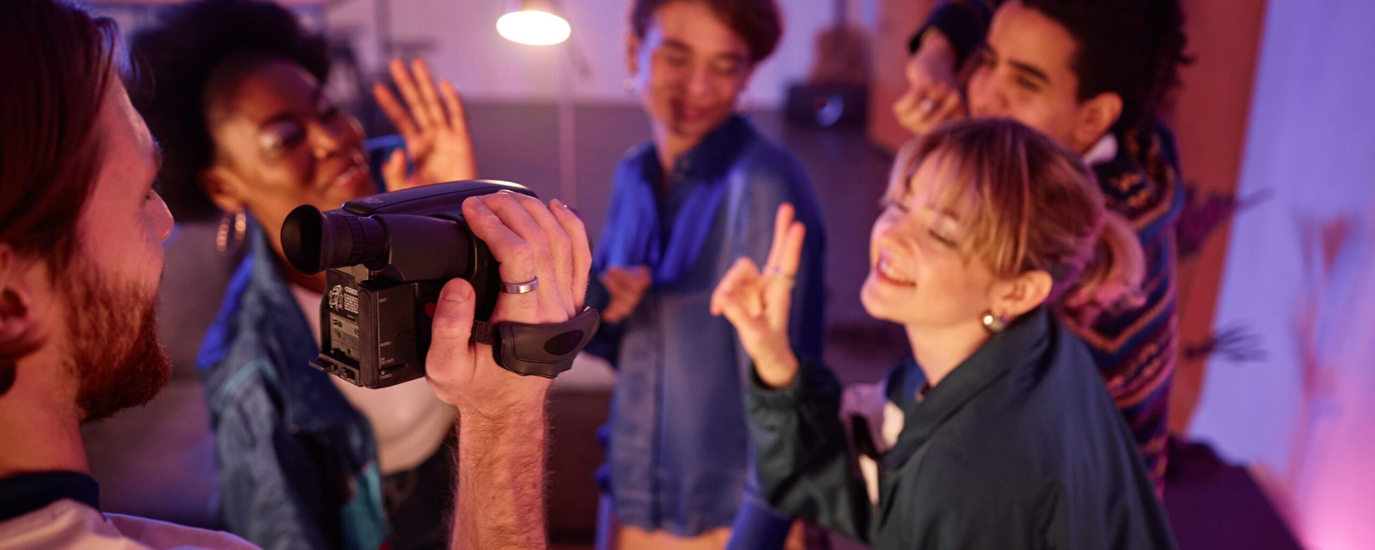Group of young people dancing at house party with man holding retro video camera and filming home video of friends having fun, copy space