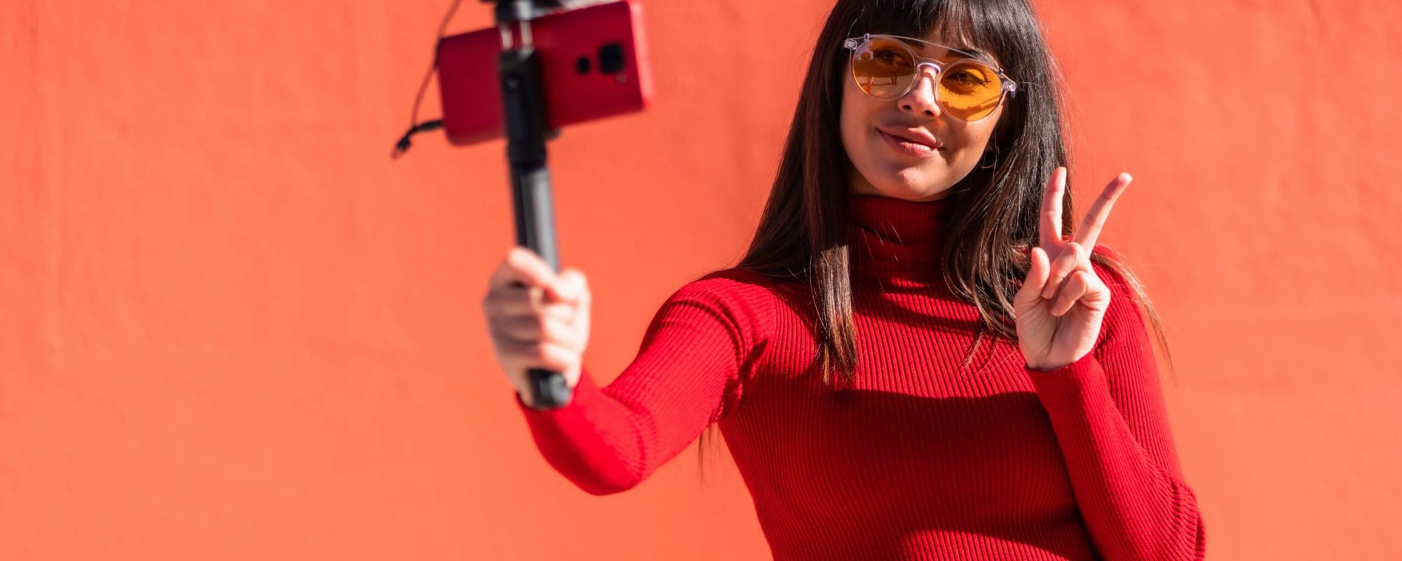 Brunette girl making the victory sign recording a video blog with the mobile