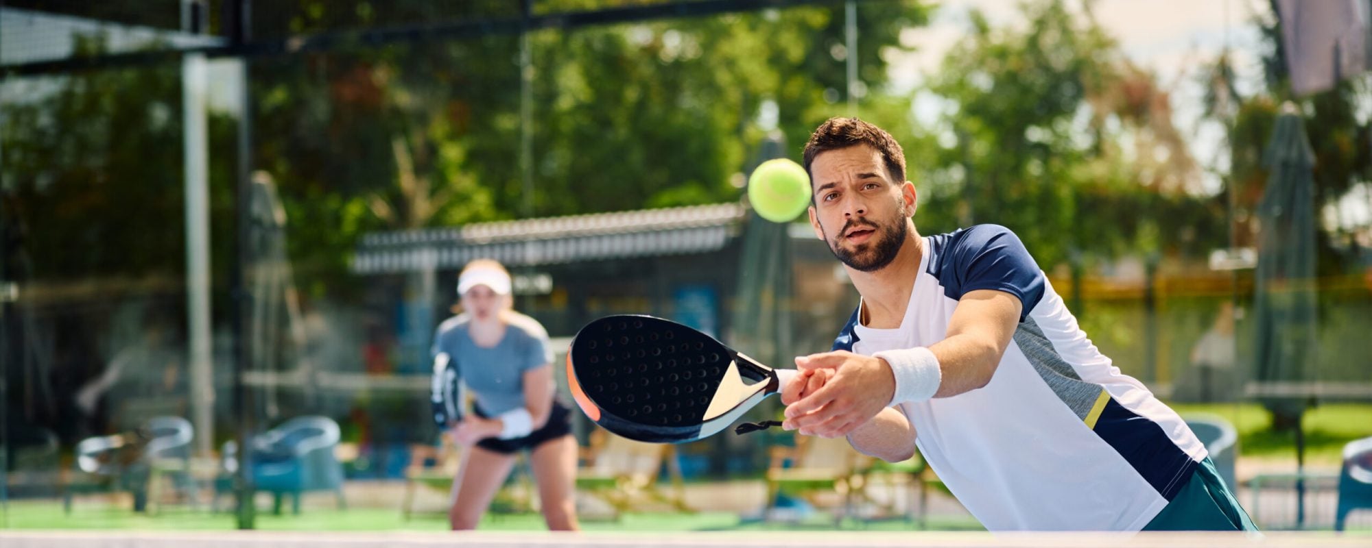 Paddle tennis player hitting the ball during mixed doubles match on outdoor court.